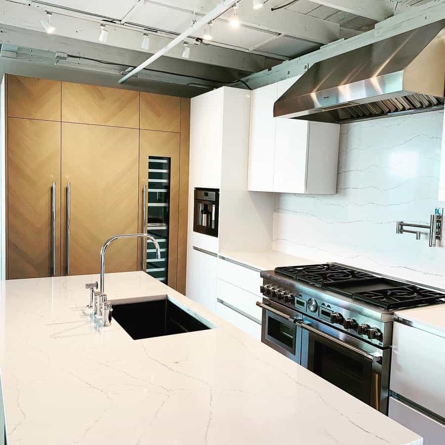 Modern kitchen with a sleek black undermount sink, high-arch chrome faucet, marble island, wood panel fridge, and professional gas range