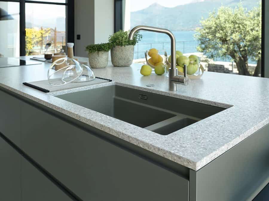 Modern kitchen island with a deep undermount sink, sleek stainless steel faucet, terrazzo countertop, and stunning lake view through large windows