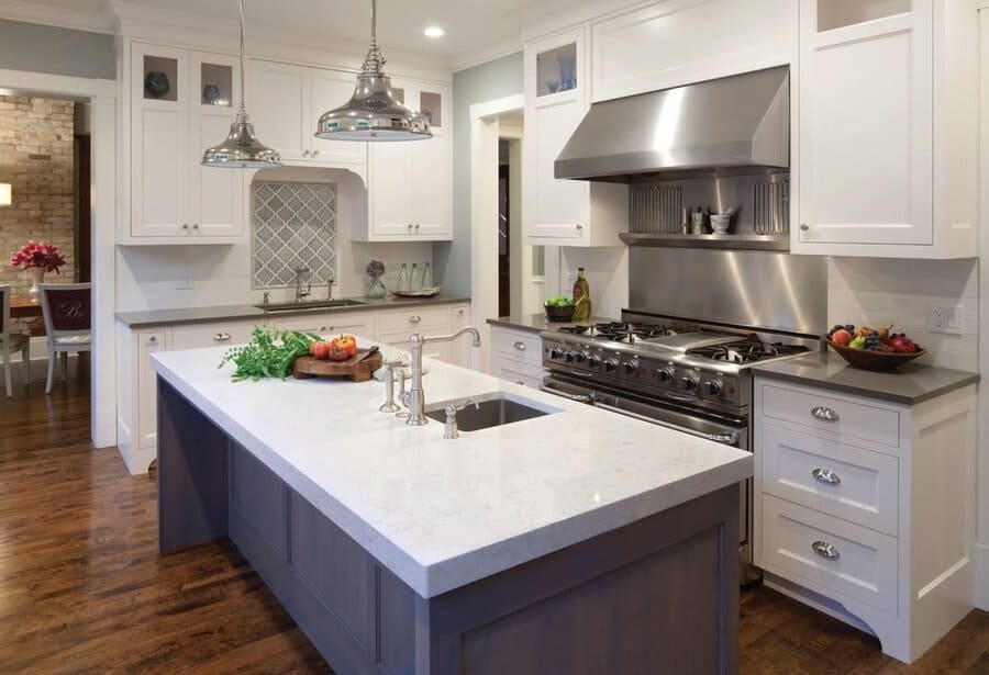 Spacious kitchen with a large island sink, quartz countertops, white cabinetry, stainless steel appliances, and industrial pendant lighting