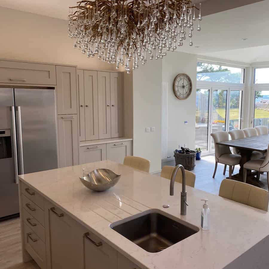 Elegant kitchen with a quartz island sink, modern faucet, neutral cabinetry, and a statement crystal chandelier adding a luxurious touch