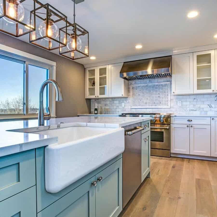 Modern farmhouse kitchen with a white apron sink, sleek high-arch faucet, soft blue island, glass pendant lighting, and marble backsplash