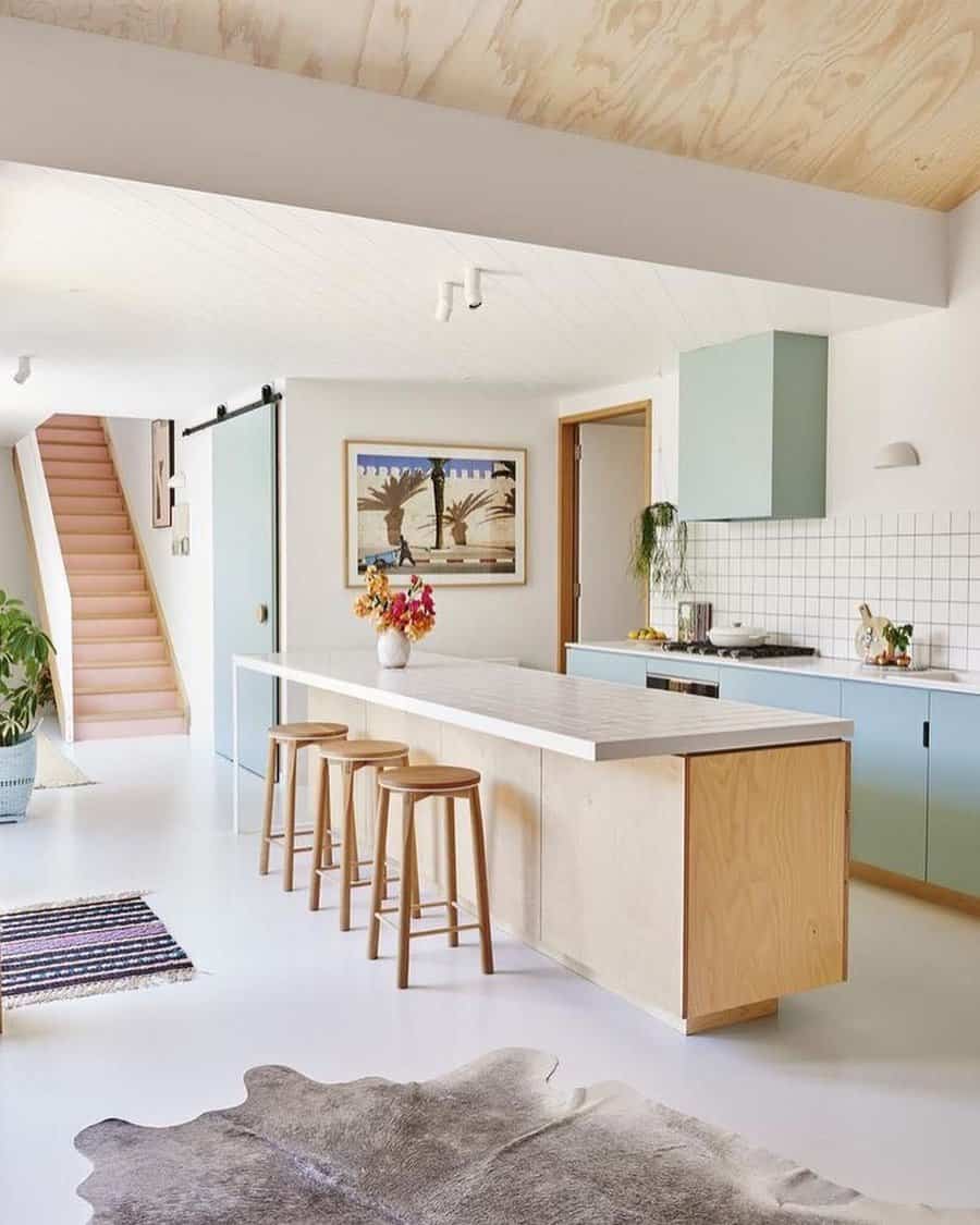 Modern kitchen with light wood tones, pastel cabinets, bar stools, and wall art