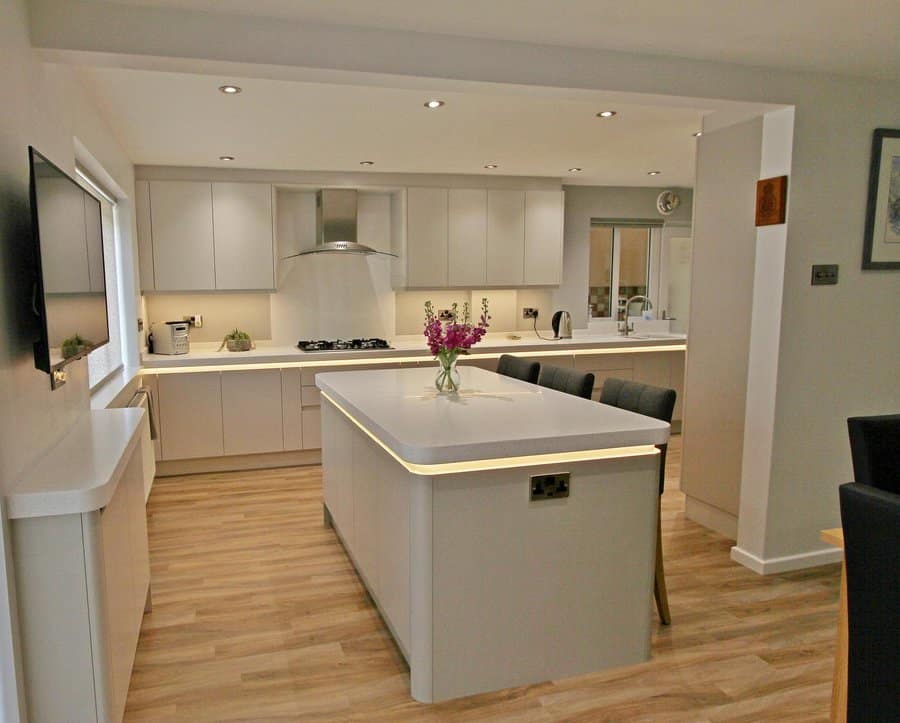 Modern kitchen with island, white cabinets, wood flooring, and a vase of flowers on the island