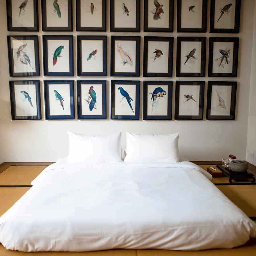 Minimalist Japanese Zen bedroom with a low platform bed, crisp white bedding, and framed bird illustrations for a serene and artistic ambiance