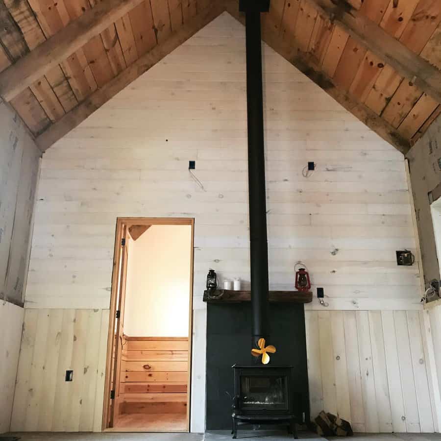 Rustic cabin-style wood stove with a tall black chimney, set against whitewashed wood walls and a vaulted ceiling for a cozy retreat feel.