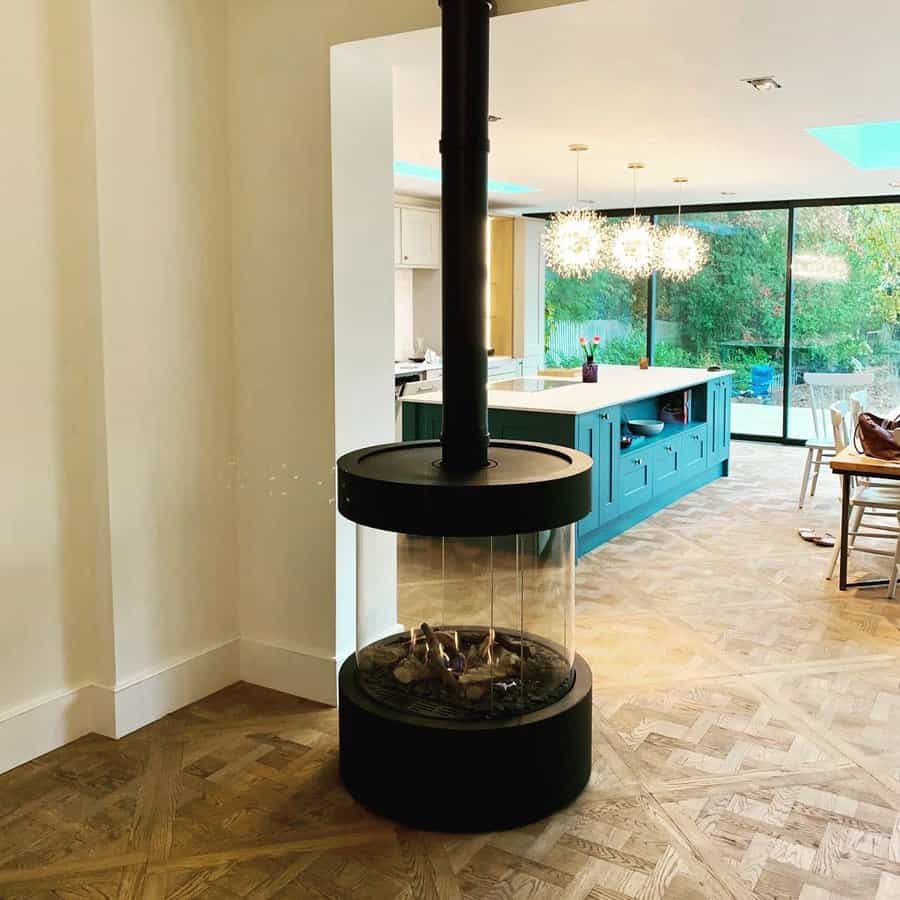 Modern suspended glass-enclosed wood stove, creating a sleek centerpiece in an open-concept space with stylish parquet flooring.