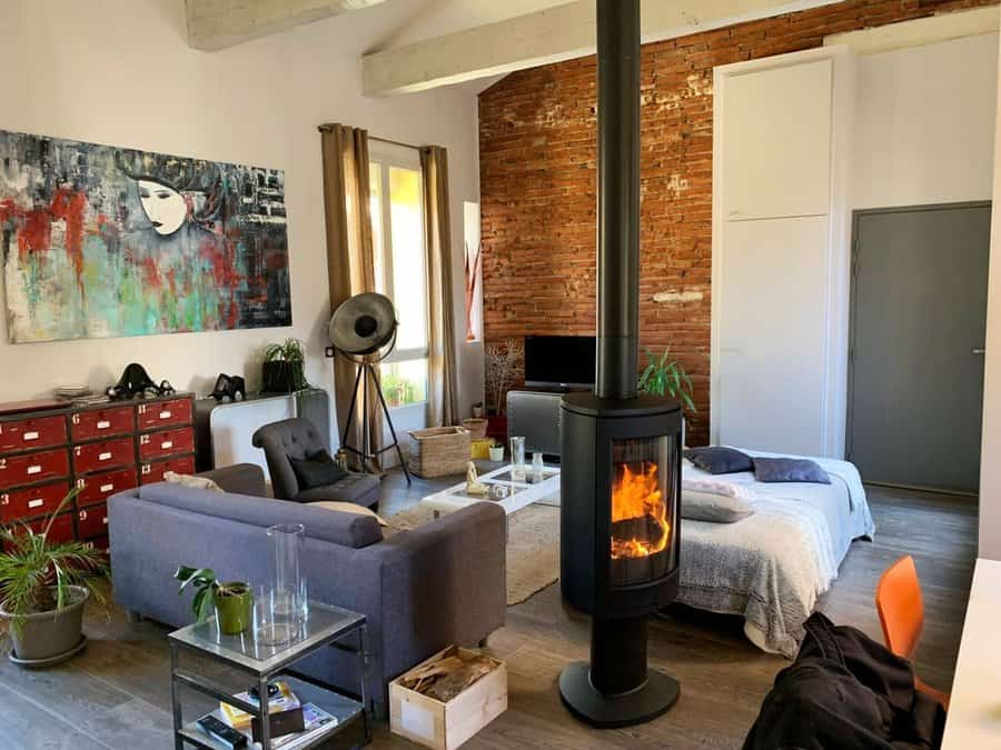 Modern freestanding wood stove in an eclectic living space with exposed brick walls, industrial decor, and cozy seating for a warm ambiance.