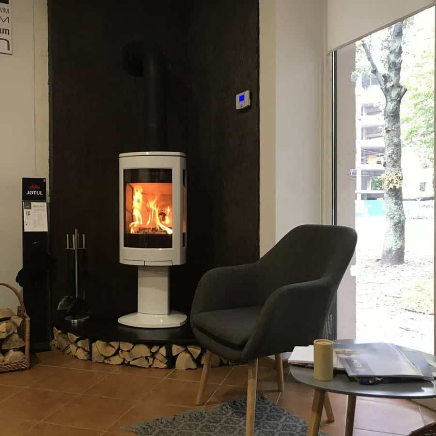 Sleek white freestanding wood stove set against a dark accent wall, with built-in log storage and cozy seating for a modern, warm ambiance.