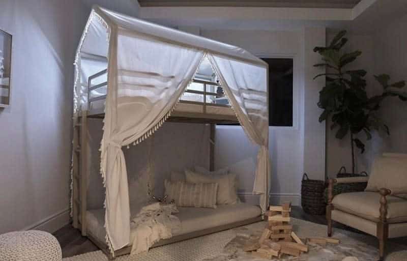 Cozy room with a bunk bed draped in white curtains, floor cushions and a wooden block stack are nearby, with a potted plant in the corner