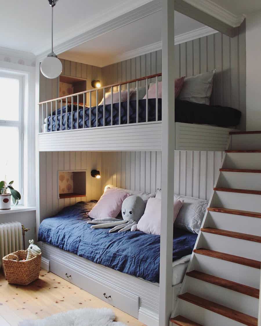 Cozy bedroom with white wood bunk beds, blue bedding, stuffed animals, stair access, a potted plant, and a wicker basket