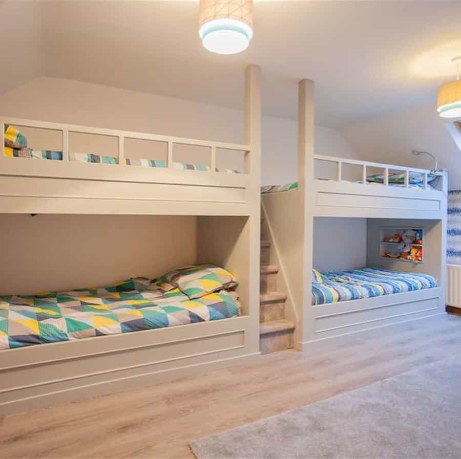 A room with two sets of white bunk beds, colorful geometric-patterned bedding, and a central staircase between them