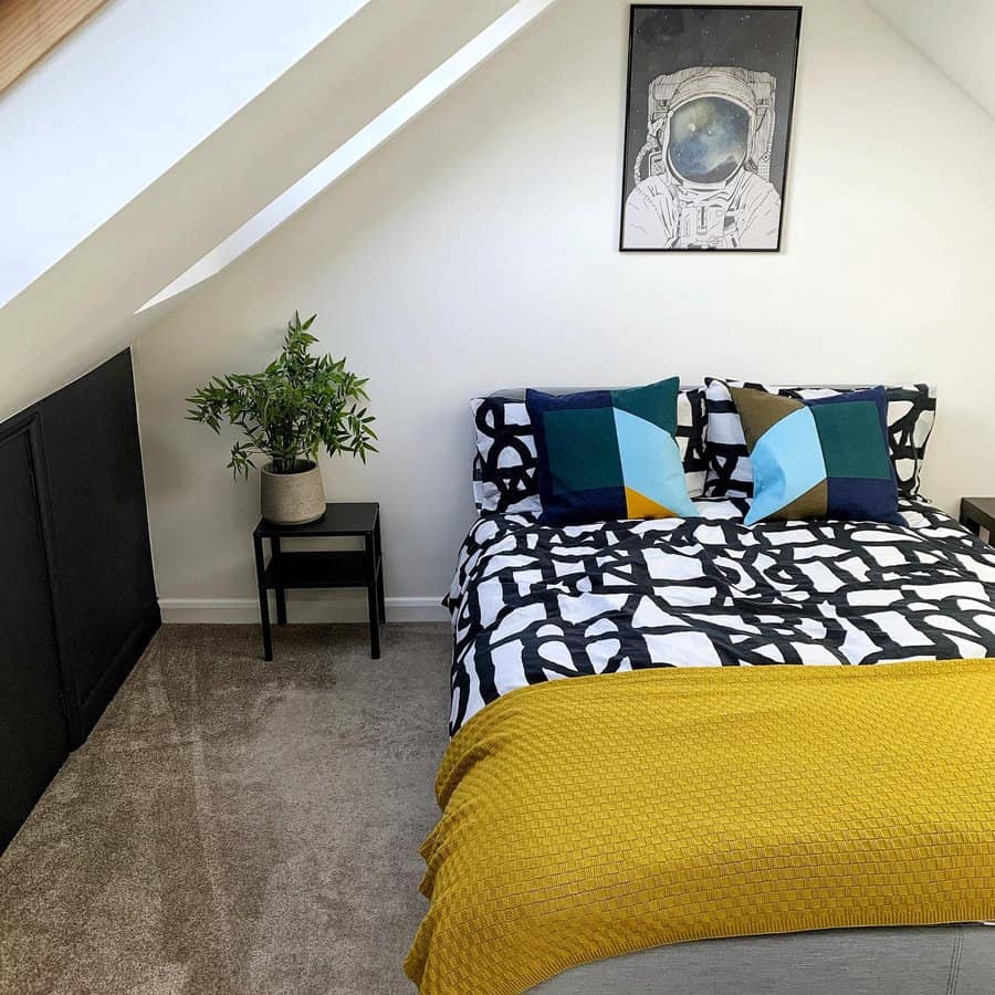 Modern attic bedroom with bold geometric bedding, a mustard throw, and space-themed decor. Skylights and sleek black accents add a contemporary touch.