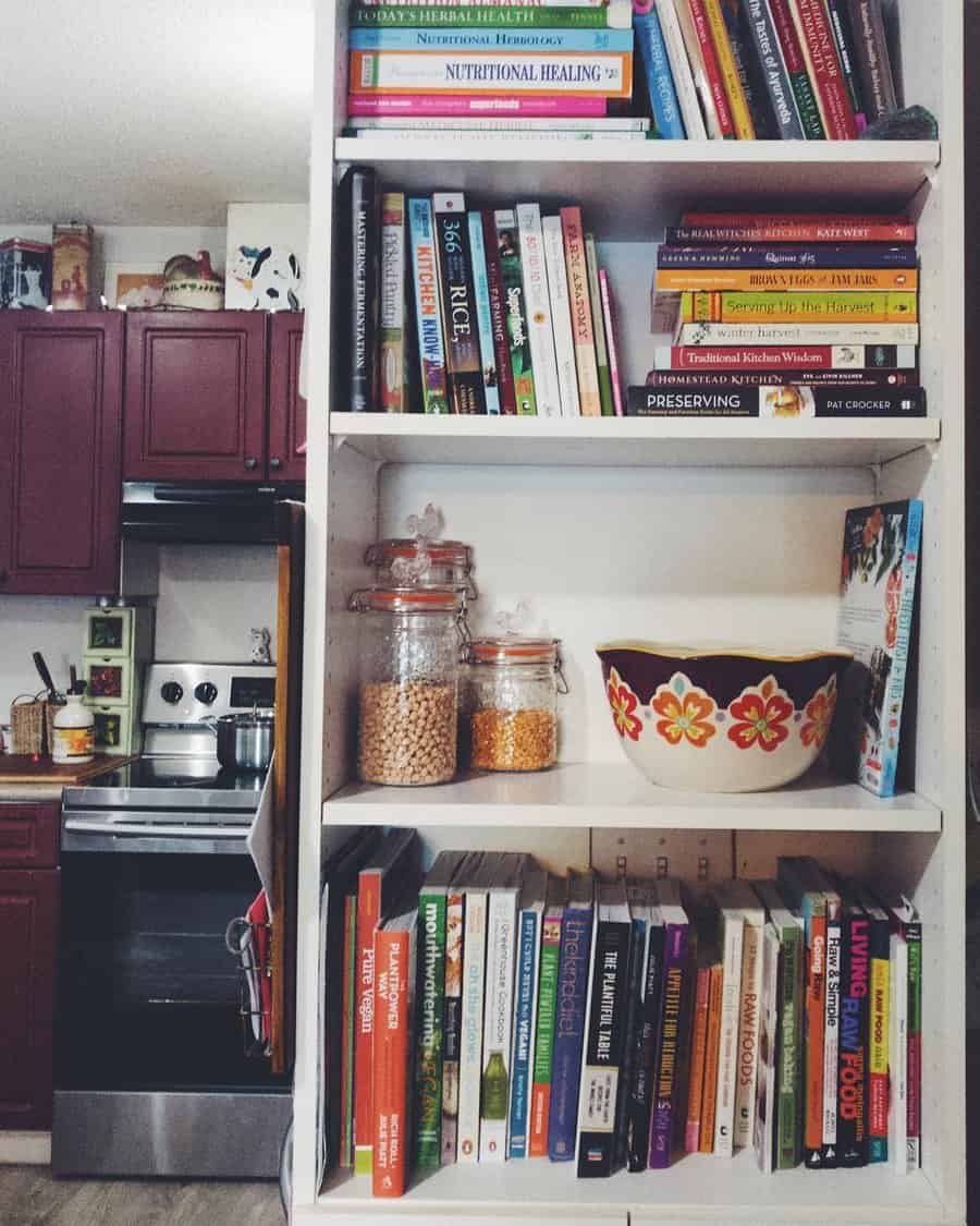 Kitchen bookshelf filled with cookbooks, nutrition guides, and food-related books, alongside glass jars and a vintage floral bowl.