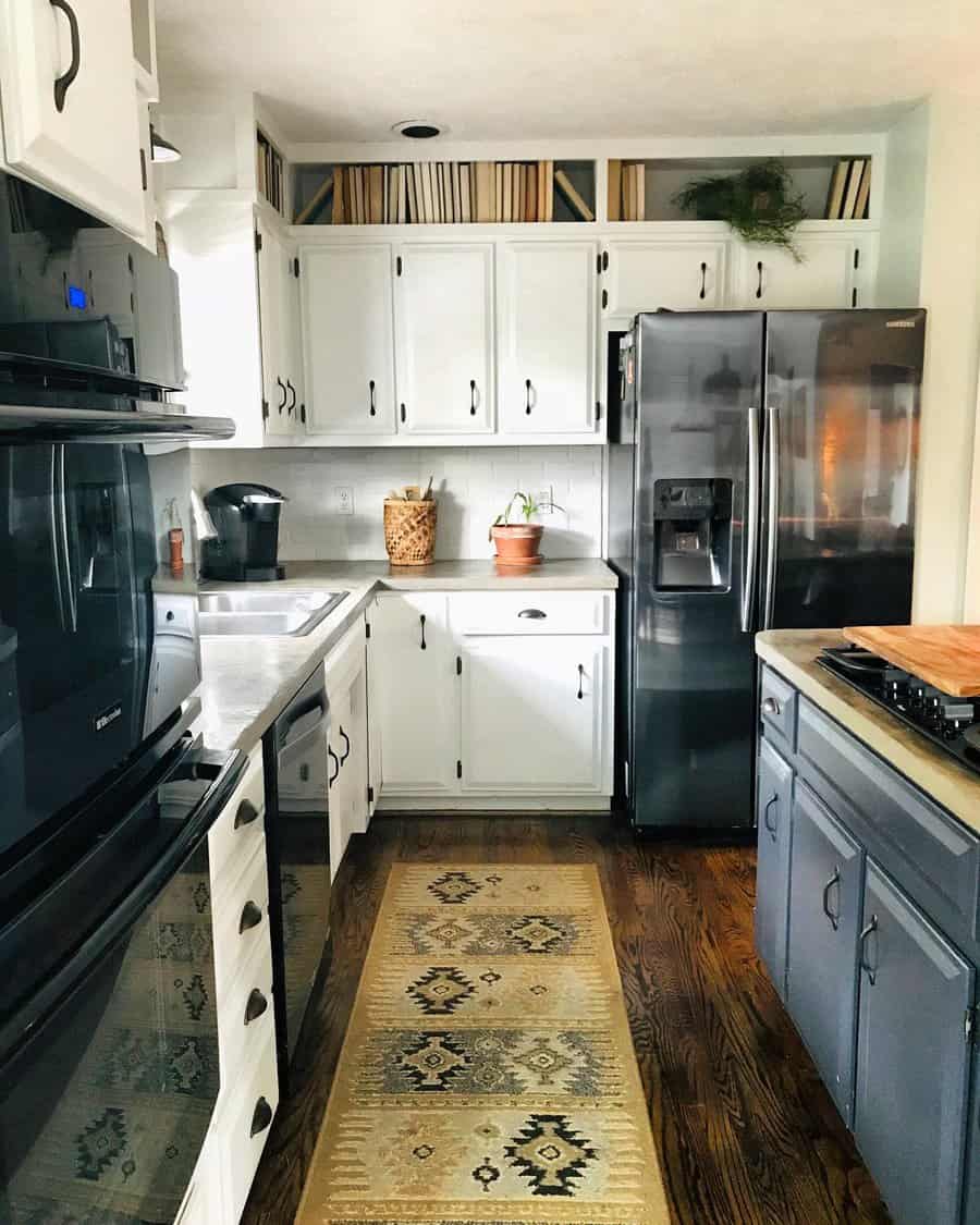 Cozy kitchen with white and navy cabinets, featuring books stored in upper open shelving above cabinets, alongside a black fridge and rustic decor.