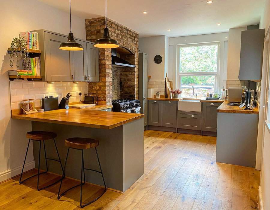 Warm industrial-style kitchen with a wooden breakfast bar, exposed brick feature, dark cabinetry, pendant lighting, and rustic barstools for a cozy feel