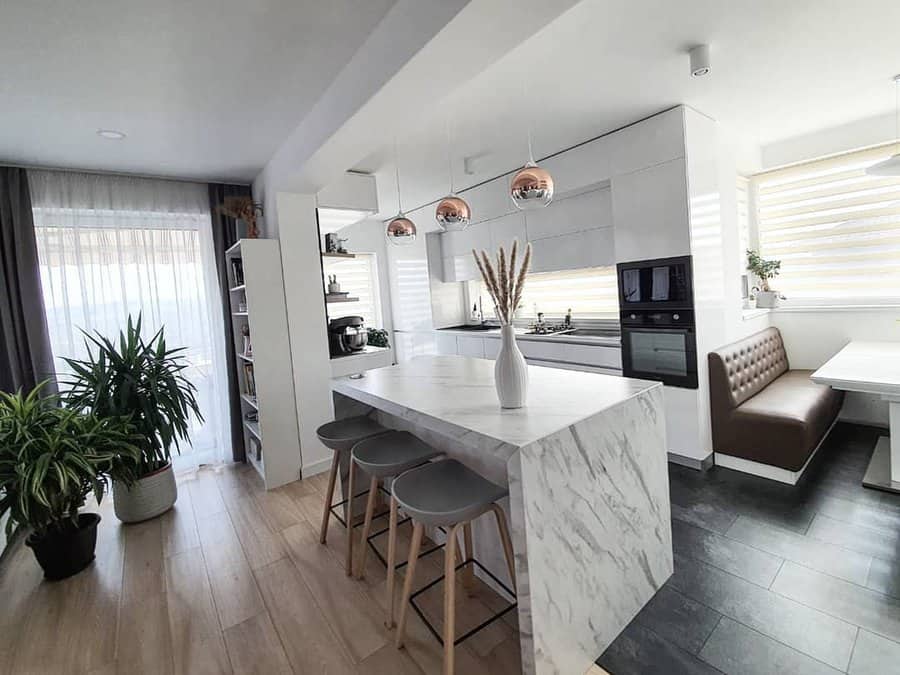 Sleek modern kitchen with a marble waterfall breakfast bar, gray barstools, copper pendant lighting, and a cozy built-in dining nook