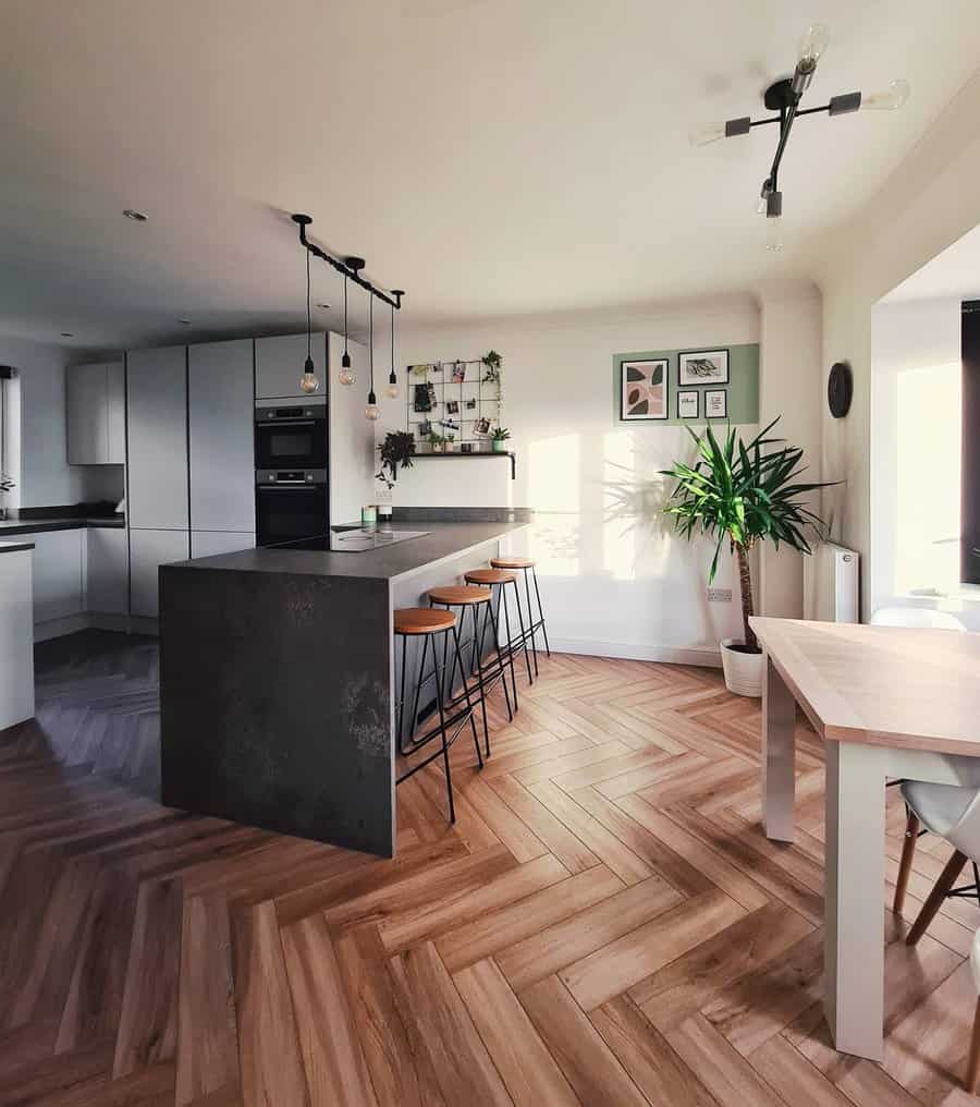 Stylish modern kitchen with a dark waterfall breakfast bar, sleek barstools, pendant lighting, herringbone flooring, and Scandinavian-inspired decor