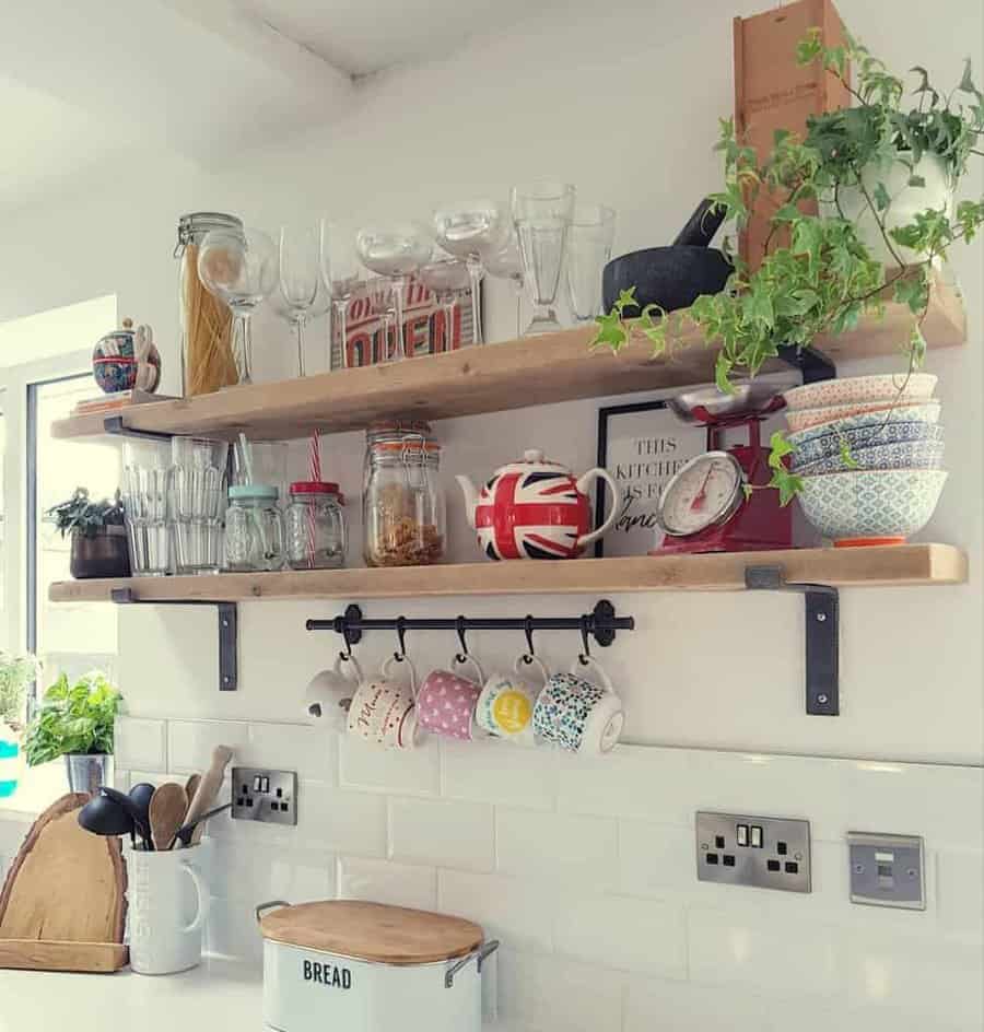 Rustic wooden floating shelves with glassware, jars, and a hanging mug rack add charm to a bright kitchen with a white subway tile backsplash