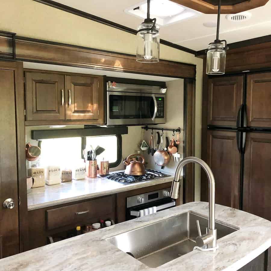 Elegant RV kitchen with dark wood cabinetry, a stainless steel sink, a gas stove, and copper cookware for a warm and functional design.