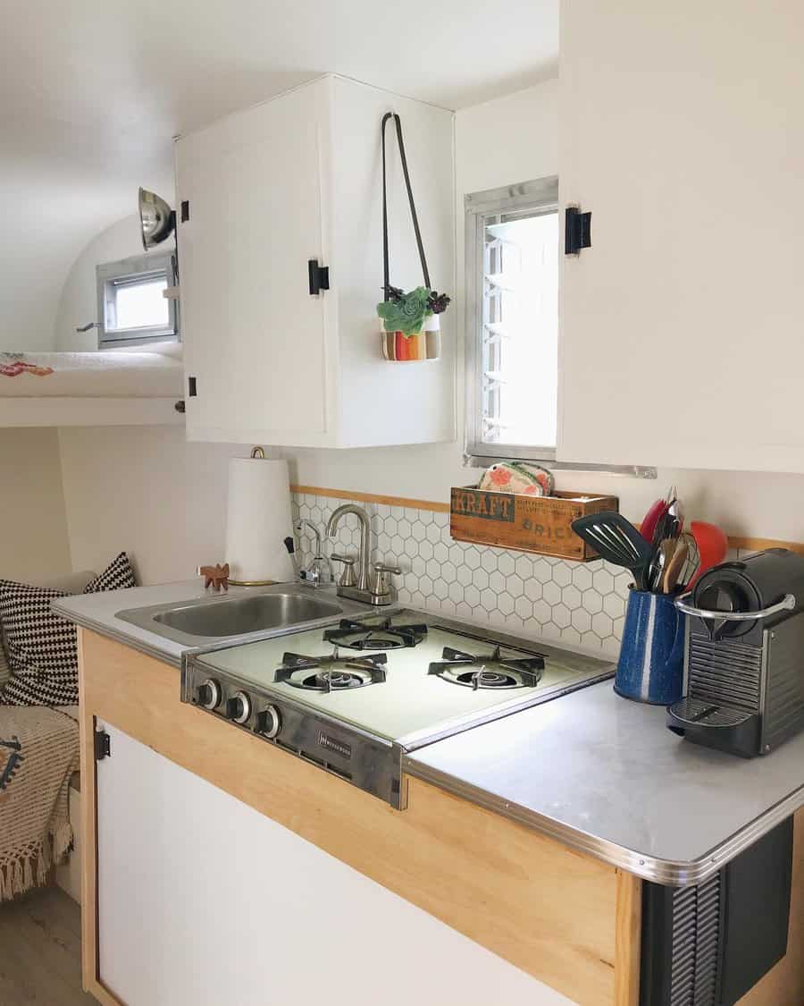 Minimalist RV kitchen with white cabinetry, a compact gas stove, a small sink, and a cozy nook, blending functionality with charm.