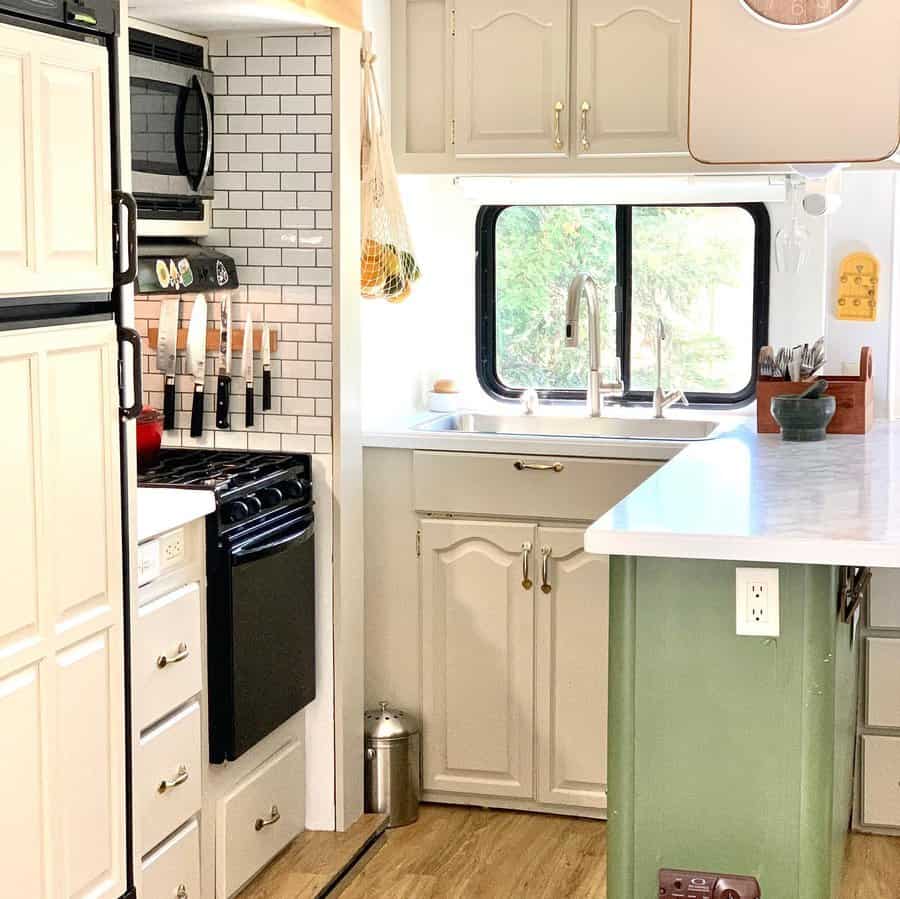 Bright RV kitchen with white cabinetry, a subway tile backsplash, a magnetic knife strip, and a farmhouse-style sink with a large window.