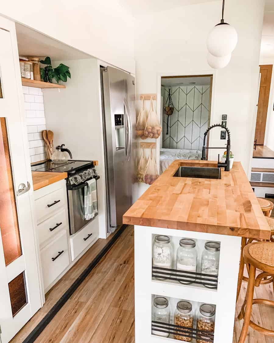 Bright RV kitchen with butcher block countertops, a farmhouse sink, open shelving, and built-in jar storage for a cozy, modern look.