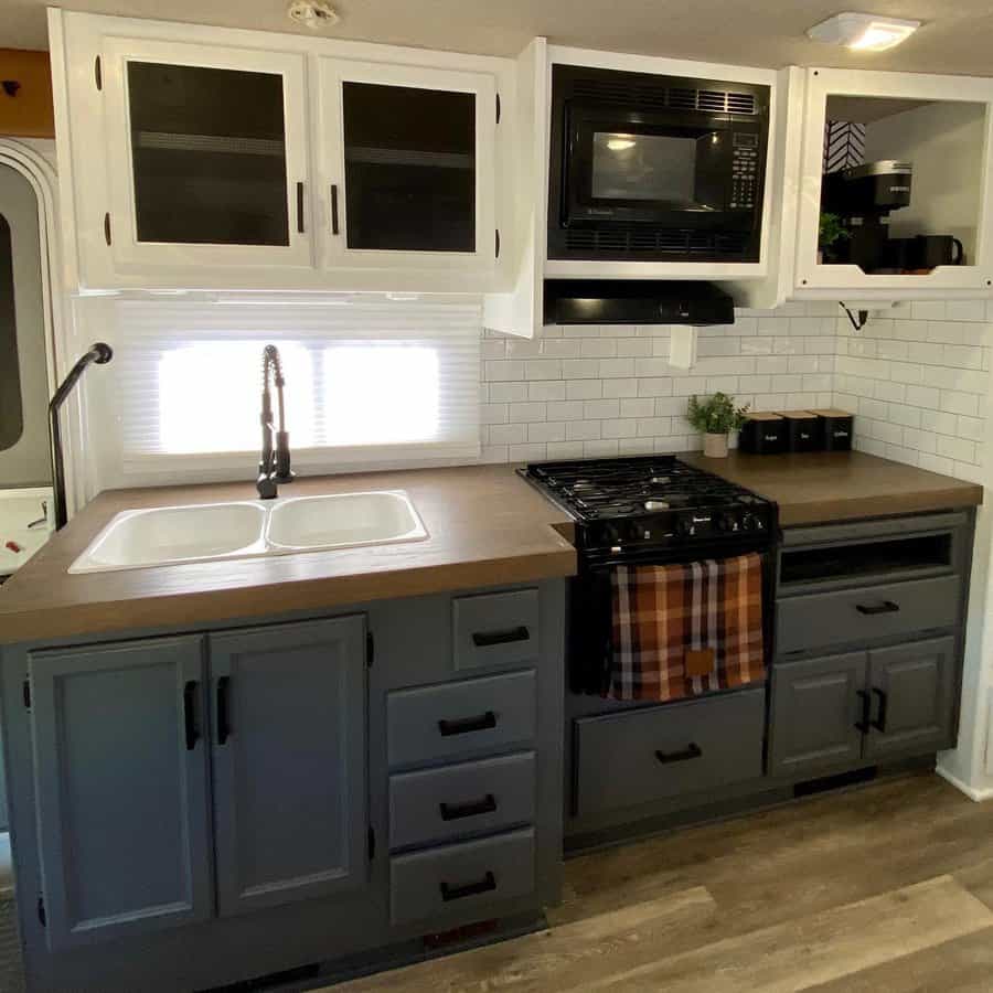 RV kitchen with two-tone cabinetry, a subway tile backsplash, a built-in microwave, and a farmhouse sink, combining style with function.