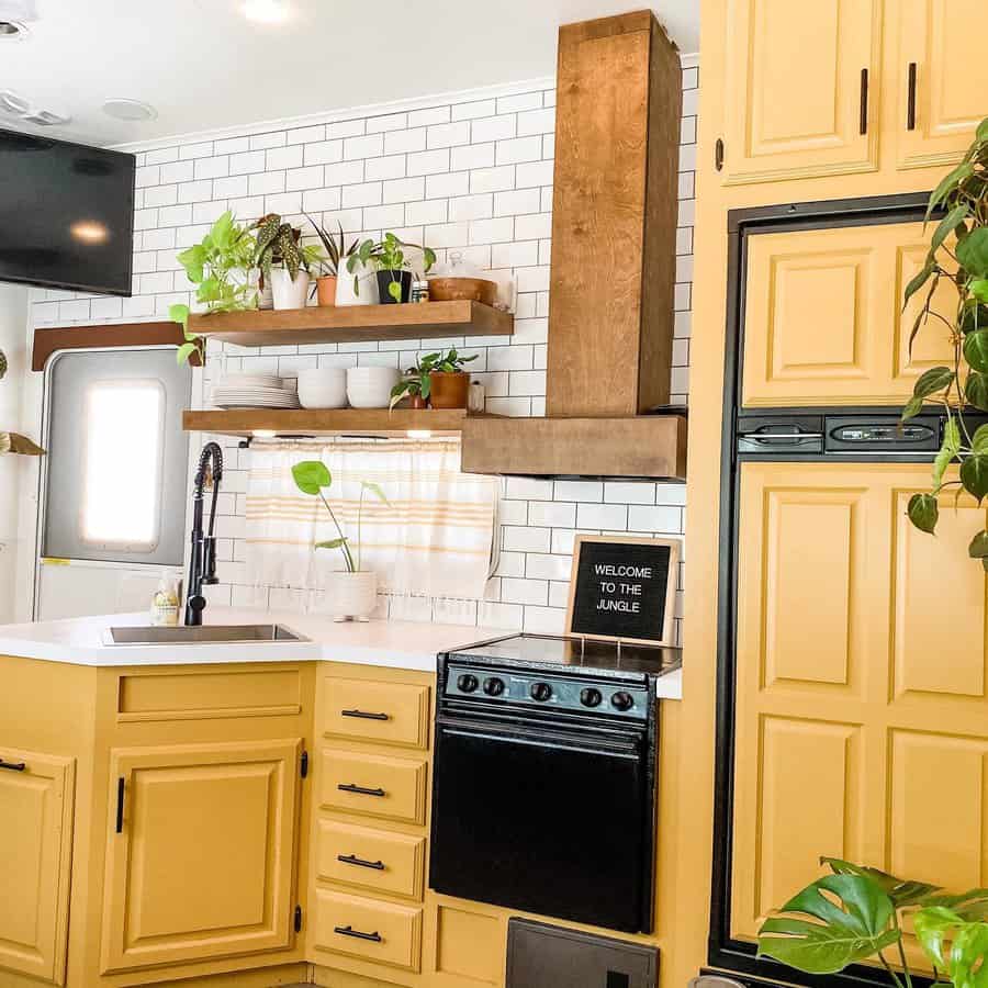 Vibrant RV kitchen with yellow cabinetry, a subway tile backsplash, open wood shelves, and greenery, creating a fresh and inviting space.