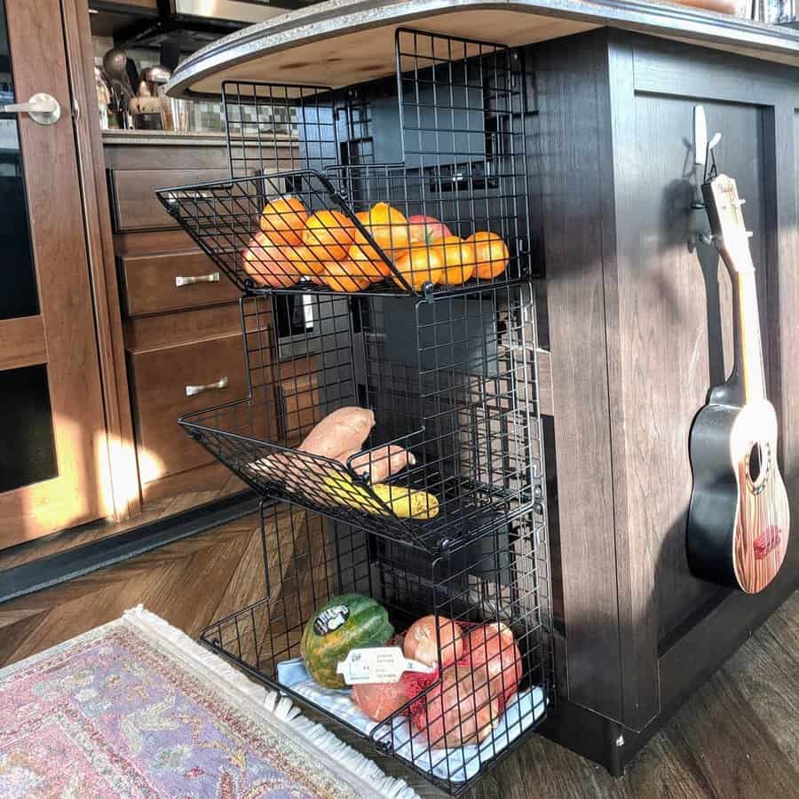 RV kitchen with a dark wood island featuring a black wire basket storage system for fresh produce, combining practicality with style.