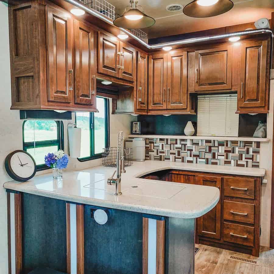 Spacious RV kitchen with rich wood cabinetry, a modern backsplash, a curved island sink, and under-cabinet lighting for a stylish look.