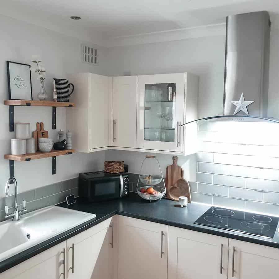 Minimalist kitchen with cream cabinets, black countertop, microwave, stove, sink, shelves with decor, and a glass fruit bowl