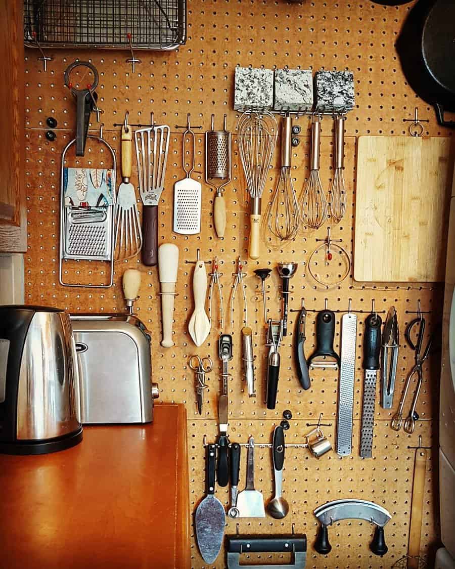 A kitchen pegboard with neatly arranged utensils, including graters, whisks, spatulas, and a toaster on a wooden counter