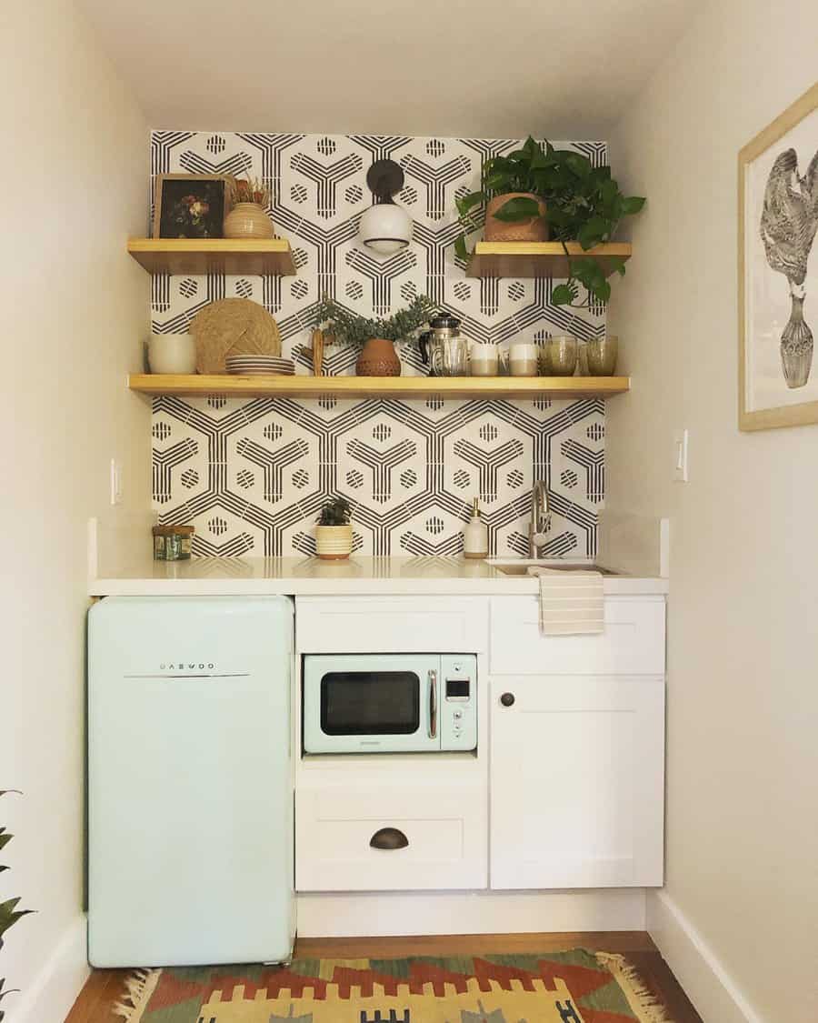 Cozy kitchenette with pastel green fridge, white cabinets, microwave, and shelves displaying plants, set against patterned wallpaper