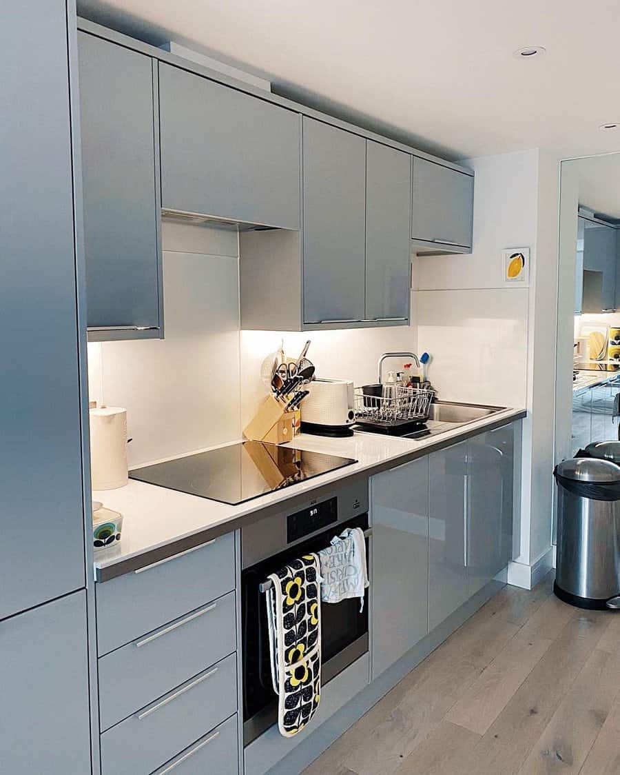 Modern kitchen with glossy grey cabinets, an electric stovetop, oven, and a countertop with a dish rack and knife block