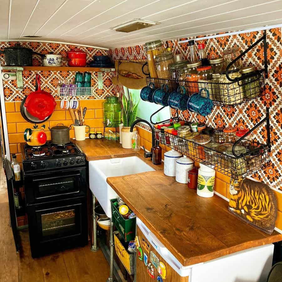 Cozy kitchen with patterned tile, wooden counters, green stove, hanging utensils, plants, jars, and a tiger cutting board