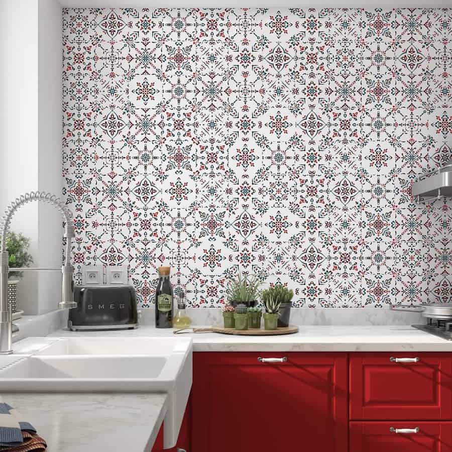 A kitchen with red cabinets, a white countertop, and patterned tiles on the wall. There are small plants and kitchen items on the counter