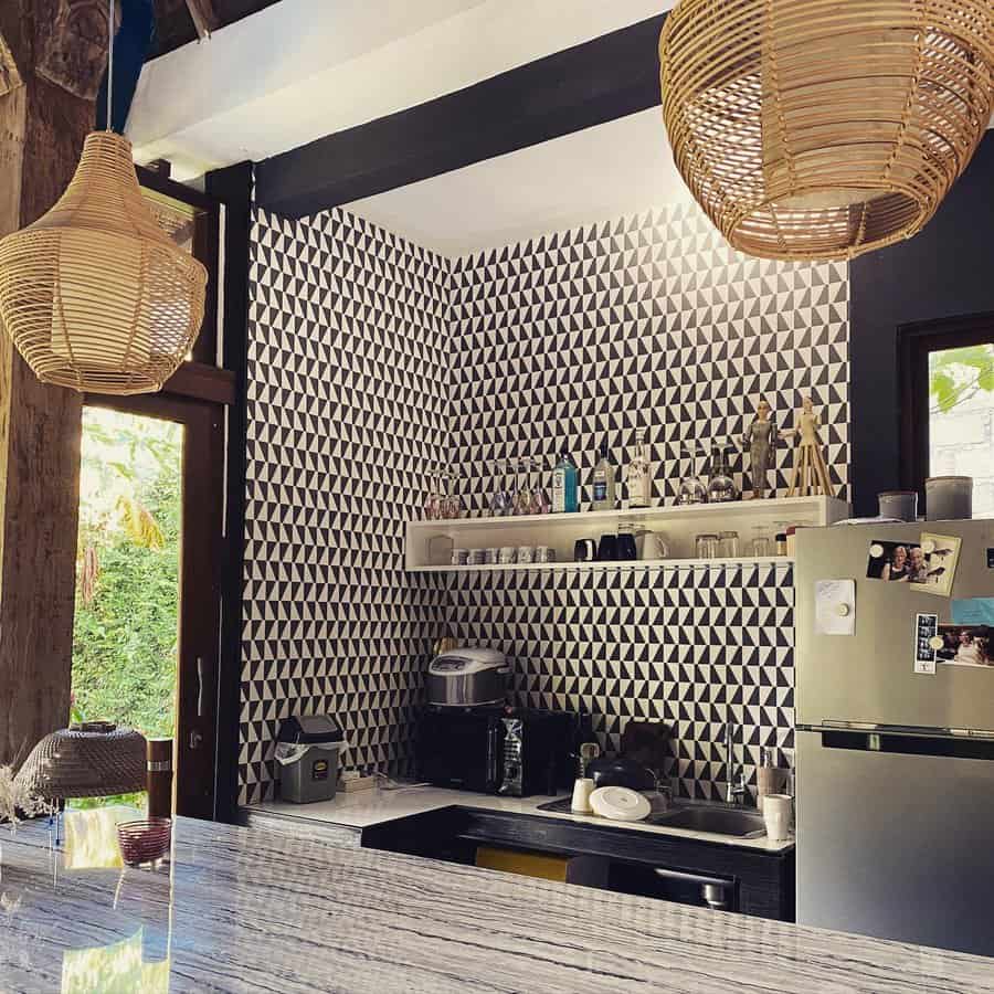 Modern kitchen with black and white geometric tile wall, wicker pendant lights, countertop appliances, and a stainless steel fridge