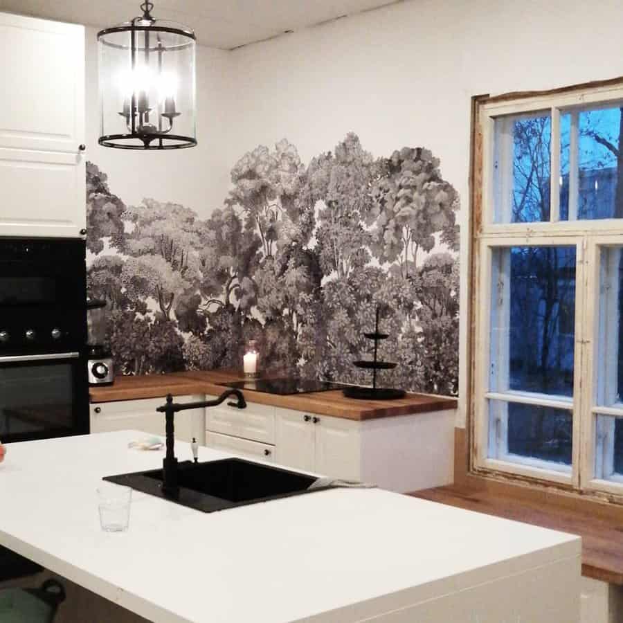 Kitchen with white cabinets, black faucet, a mural of trees, and a large window with a candle lit by the mural