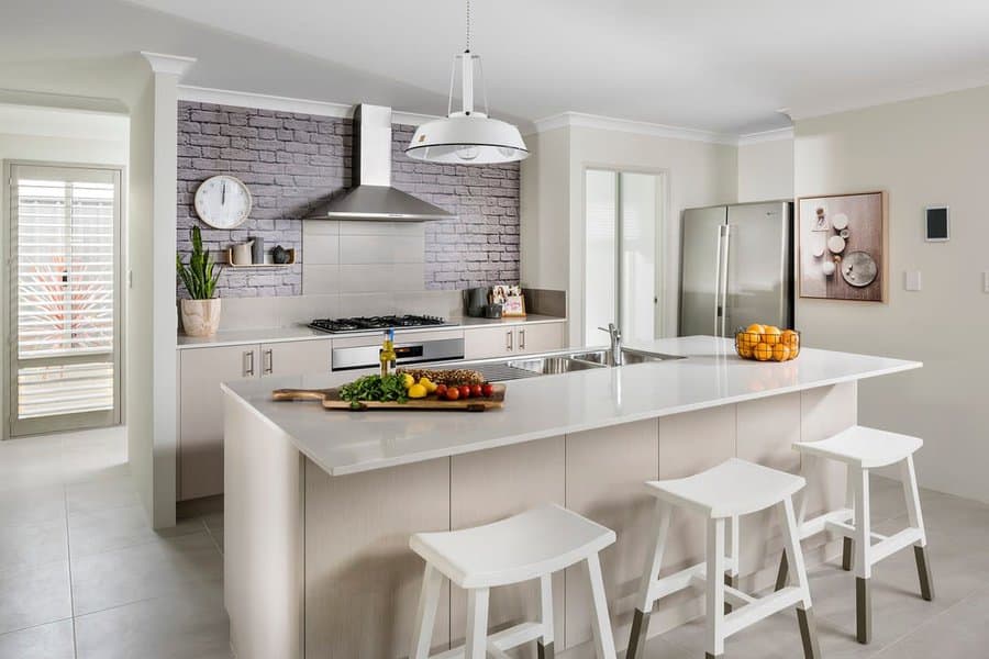 Modern kitchen with white cabinetry, island with stools, stainless steel appliances, and brick backsplash featuring a bowl of oranges on the counter