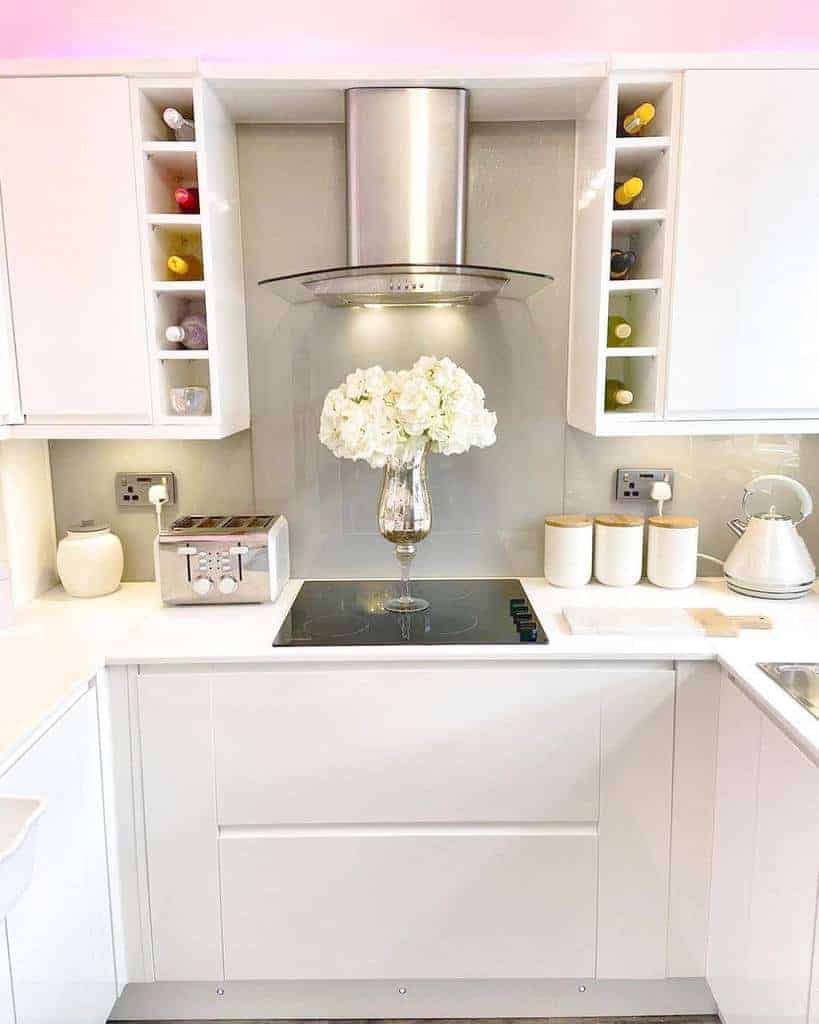 Modern white kitchen with built-in wine racks, sleek cabinetry, and a glass cooktop, accented by a floral centerpiece for elegance