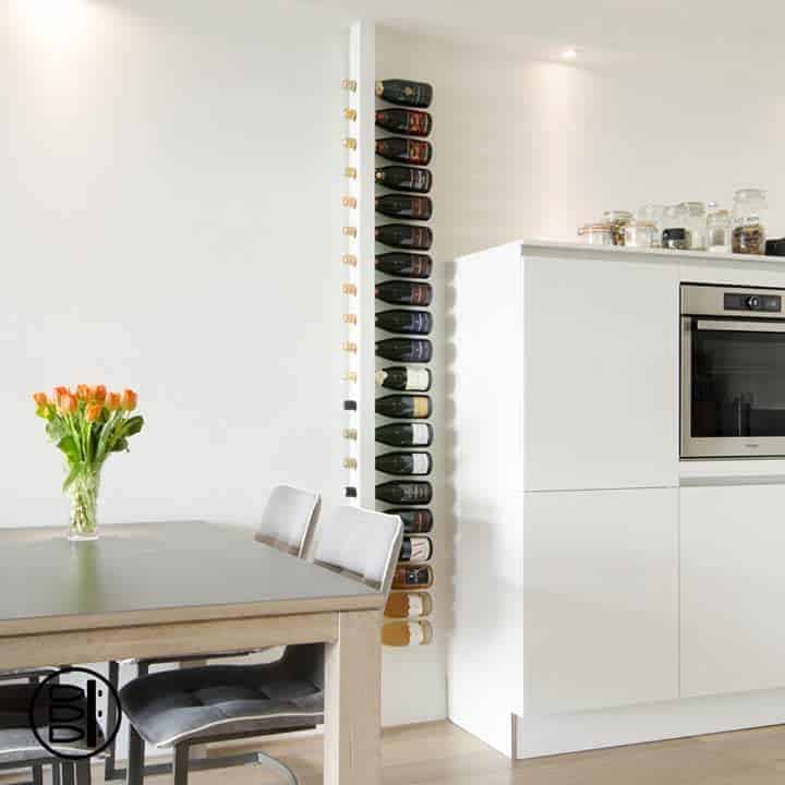 Modern kitchen with a vertical wine rack, white cabinets, built-in oven, and a dining table with orange tulips in a vase