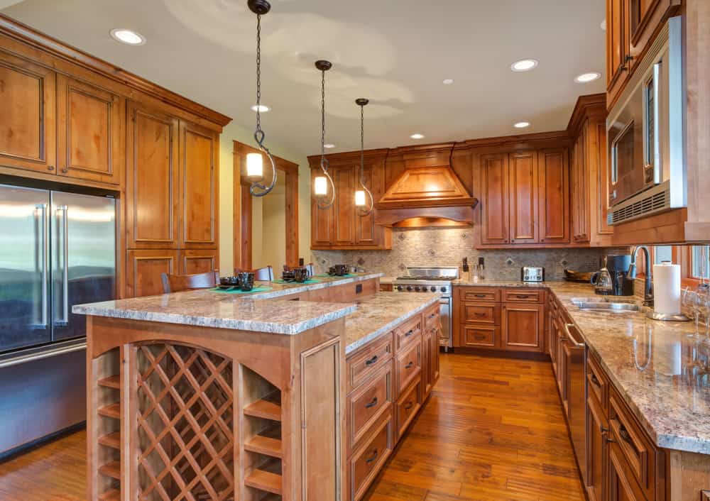 Spacious kitchen with wooden cabinets, a large island with wine rack, pendant lights, stainless steel appliances, and wooden floors