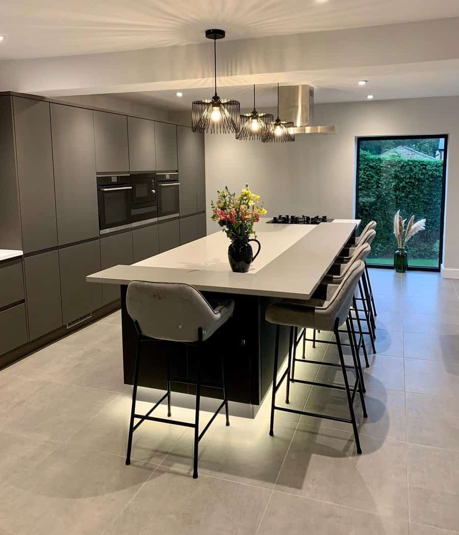 Sophisticated kitchen with an L-shaped breakfast bar, sleek black cabinetry, plush barstools, statement pendant lighting, and under-island LED glow