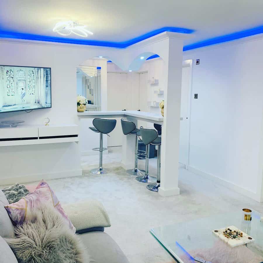 Modern L-shaped breakfast bar in an open-plan living space, featuring sleek gray barstools, white countertops, and ambient blue LED ceiling lighting