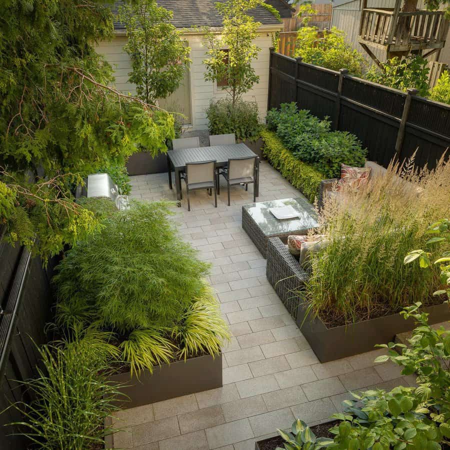 Modern backyard with sleek stone pavers, lush greenery in raised planters, a cozy seating area, and a stylish dining space for outdoor relaxation