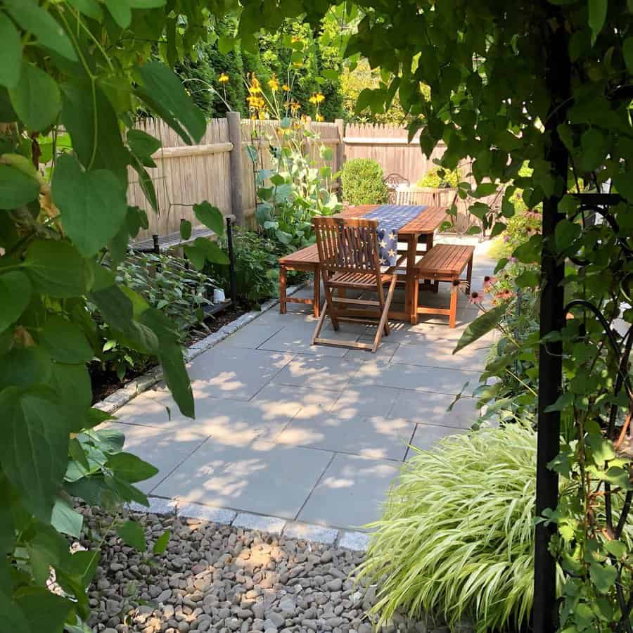 Charming garden patio with stone pavers, a wooden dining set, lush greenery, and a bamboo fence creating a cozy, secluded outdoor retreat