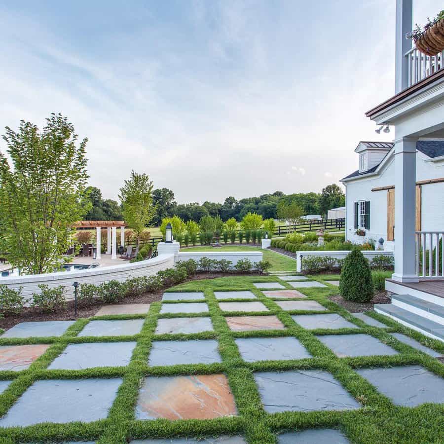 Expansive low-maintenance landscape design featuring a checkerboard pattern of grass and stone tiles, paired with trimmed hedges, a pergola seating area, and lush greenery for a balanced and elegant outdoor space