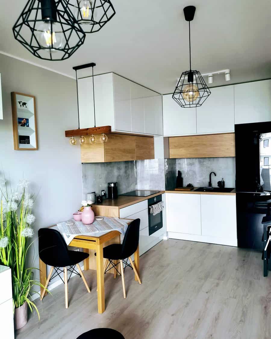 Light wood flooring adds warmth and contrast to this modern kitchen, complementing white cabinetry, black accents, and industrial lighting