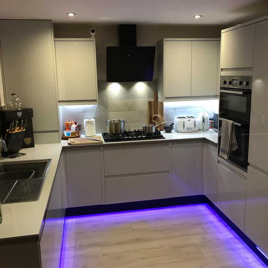 Light wood flooring enhances this sleek modern kitchen, complemented by ambient LED lighting, neutral cabinetry, and a clean, minimalist design