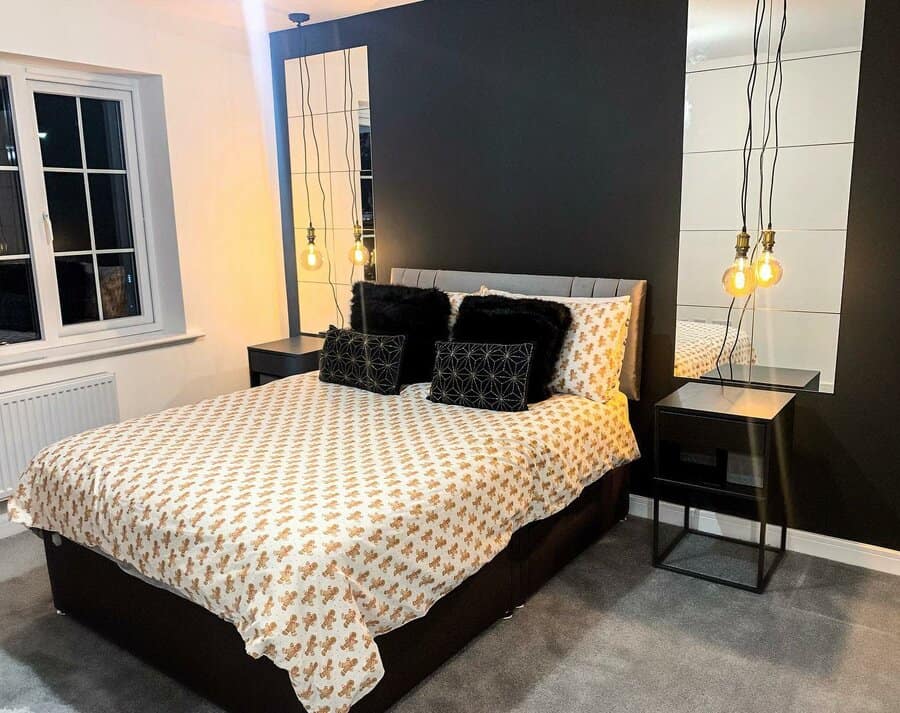 Modern bedroom with a black accent wall, bed with geometric-patterned bedding, dual pendant lights, side tables, and a window